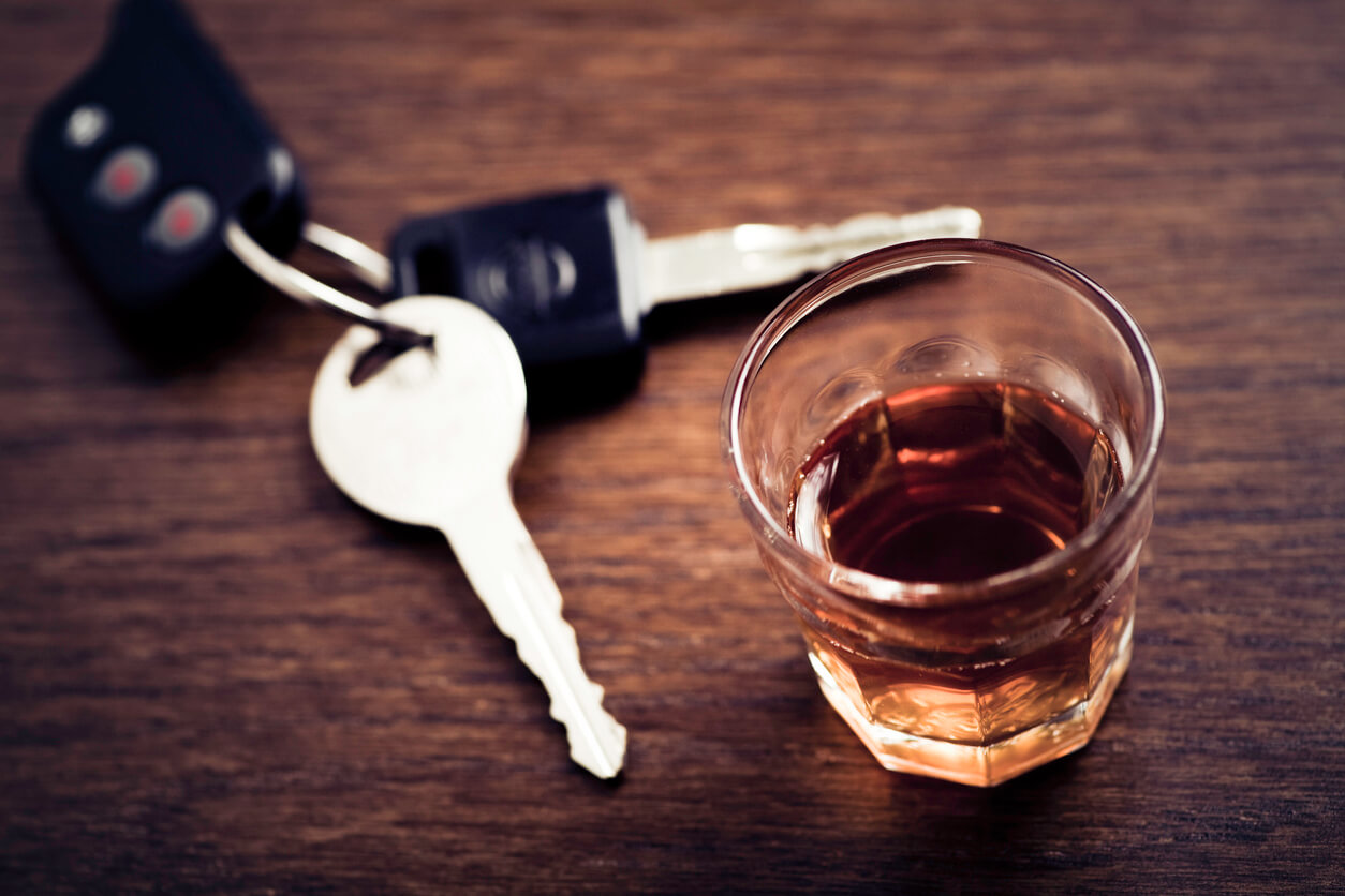 A sharp image depicting a set of car keys next to a small glass of whiskey on a wooden table, suggesting the important decision not to drink and drive.