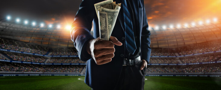 businessman holding large amount of bills at Soccer stadium in background